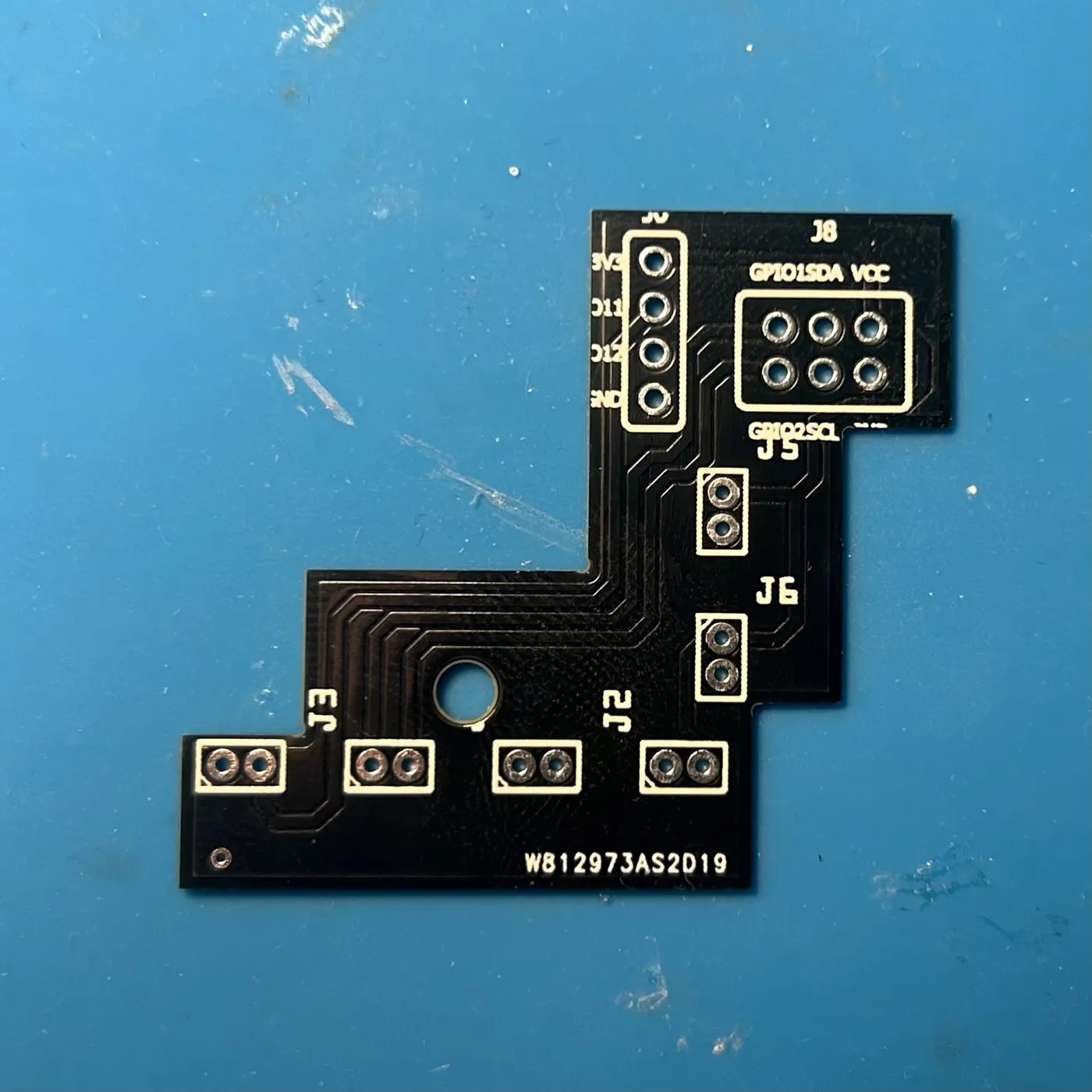 The fabricated addon board, unpopulated. The 2x3 field at the top right lands on J8 with its GPIO1, SDA, VCC, GPIO2 and SCL labels; the four-hole row to its left lands on J6; the six 2-pin footprints along the lower arm are the sockets.