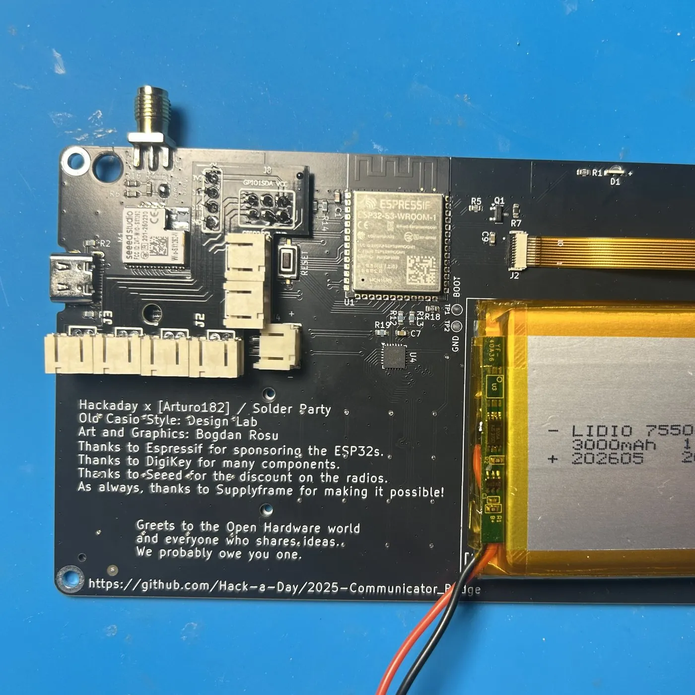 The addon board soldered onto the badge back, its JST sockets standing proud of the board, next to the ESP32-S3 module and the LiPo pack.